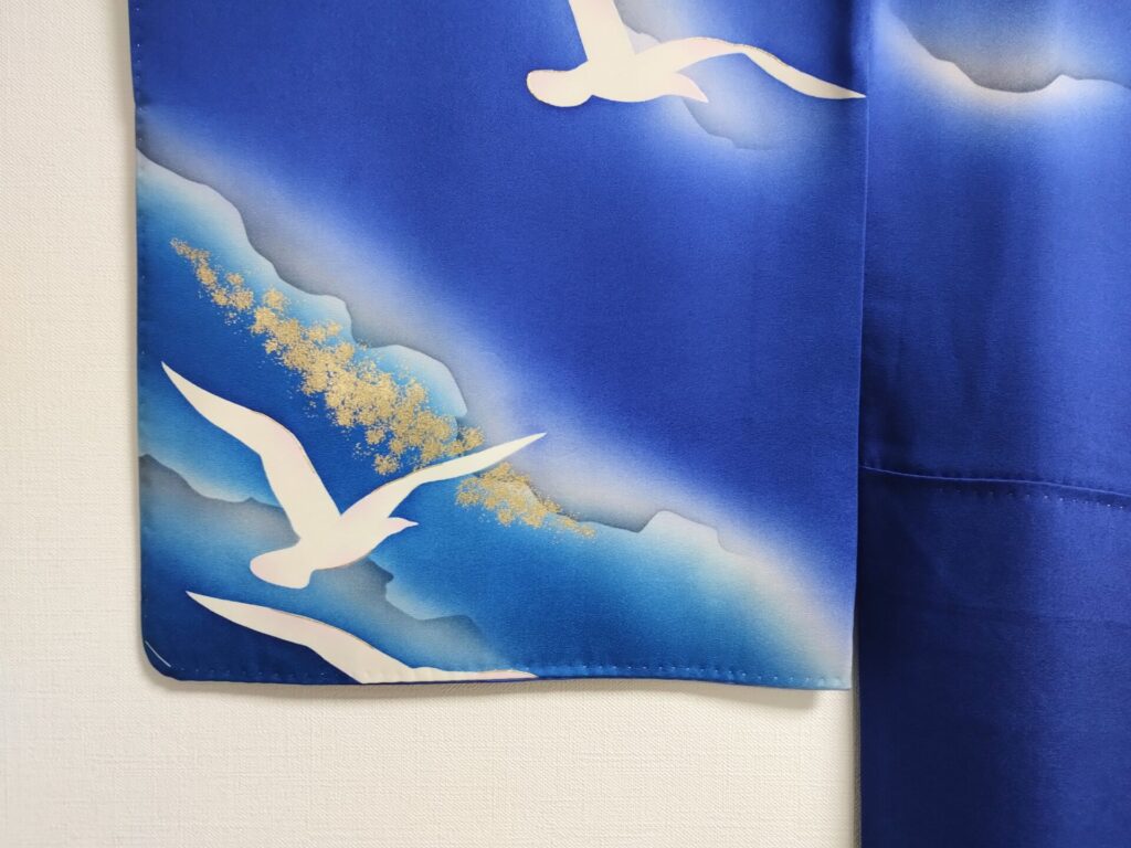 青い着物の袖に白い鳥が飛ぶ模様が描かれている
